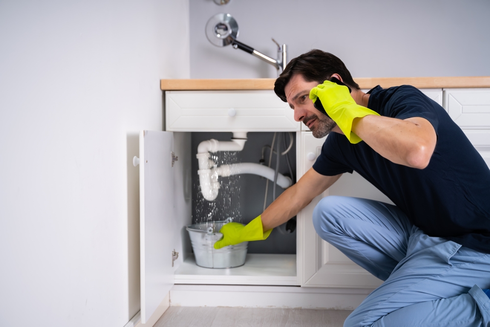 Sad,young,man,calling,plumber,in,front,of,water,leaking